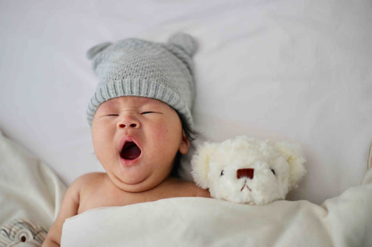 baby yawning in bed with hat and teddy bear