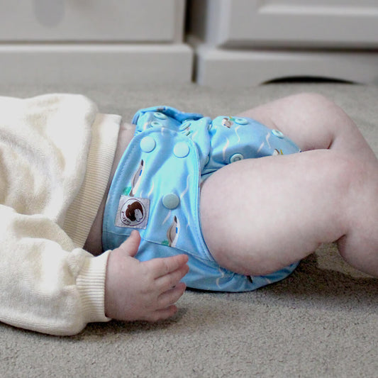 A baby lying on the floor wearing a blue cloth nappy with ducks on.
