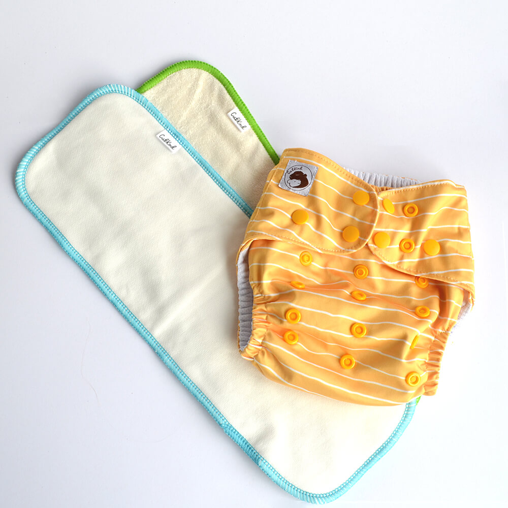 A yellow cloth with white stripes sitting on a cotton insert with blue binding and a bamboo insert with green binding.