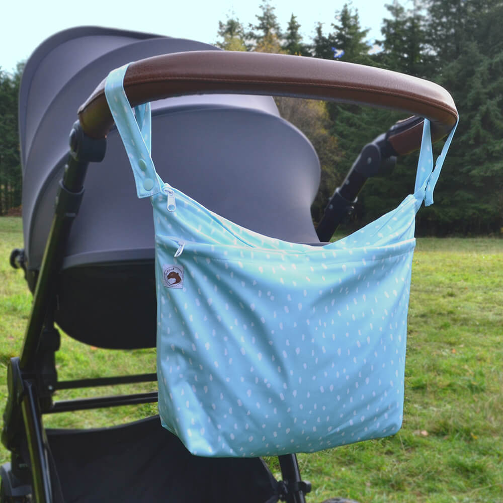 A large wetbag in 'soft skies' design, hanging on the handle of a pushchair.