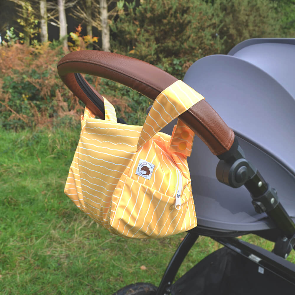 A yellow nappy pod with white stripes, hanging on the handle of a pushchair.